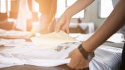 Young woman pull out paper from waterproof film on fabric at shop. worker working on manual screen printing on t-shirt. Promotional Printing
